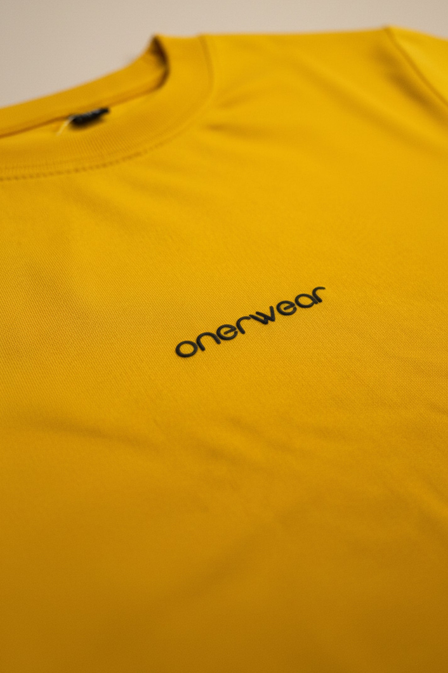 Yellow shirt with 'onerwear' logo on a beige background