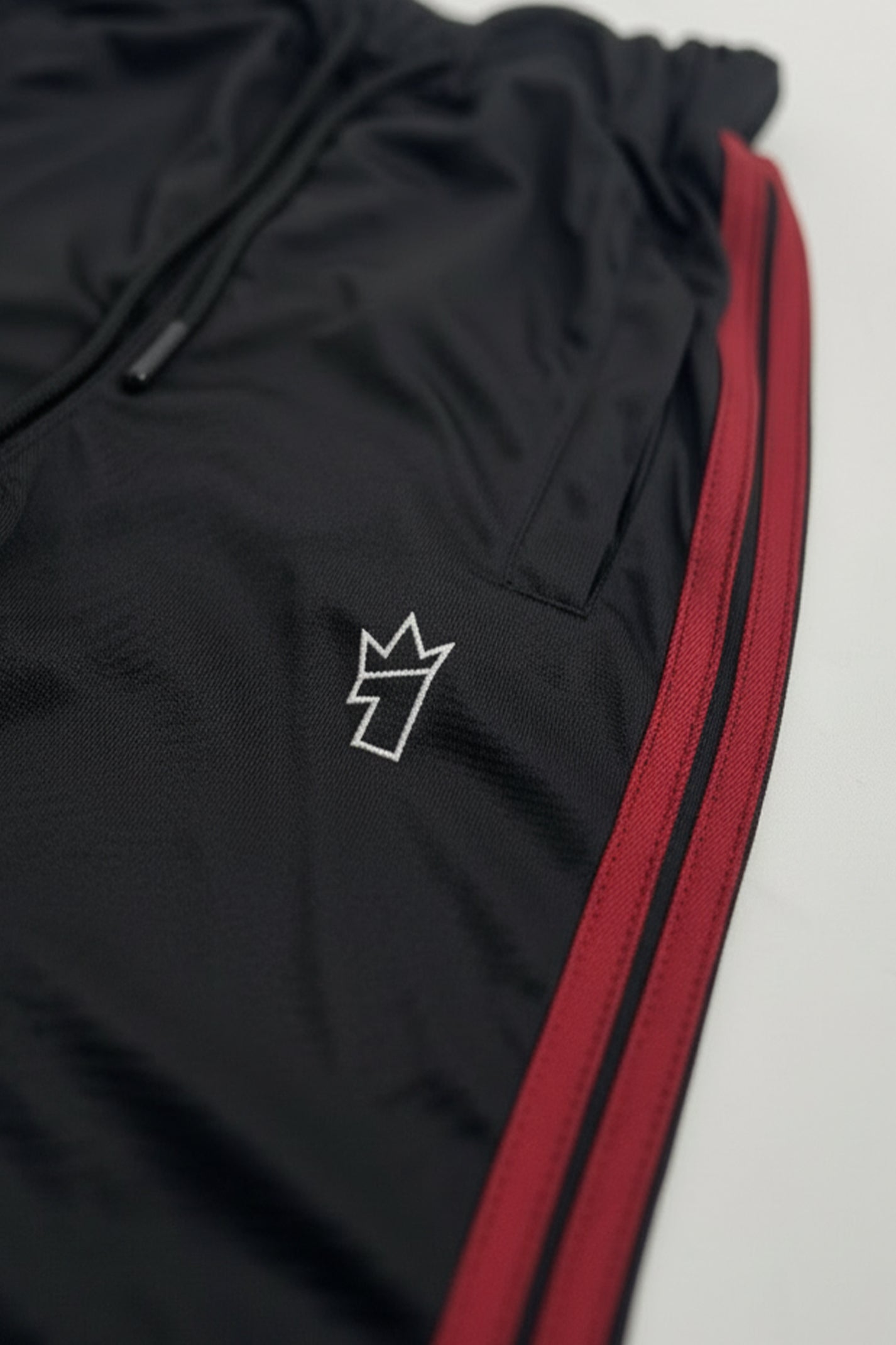 Black tracksuit with red side stripe on a light gray background