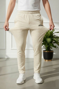 Person wearing beige pants with a logo, standing indoors next to a plant.