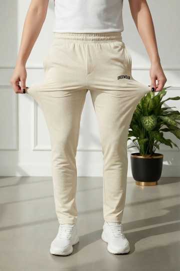Person wearing beige pants with a logo, standing indoors next to a plant.