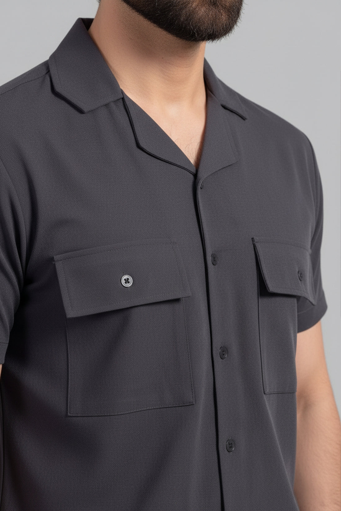 Close-up of a dark gray short-sleeve shirt with two front pockets on a neutral background