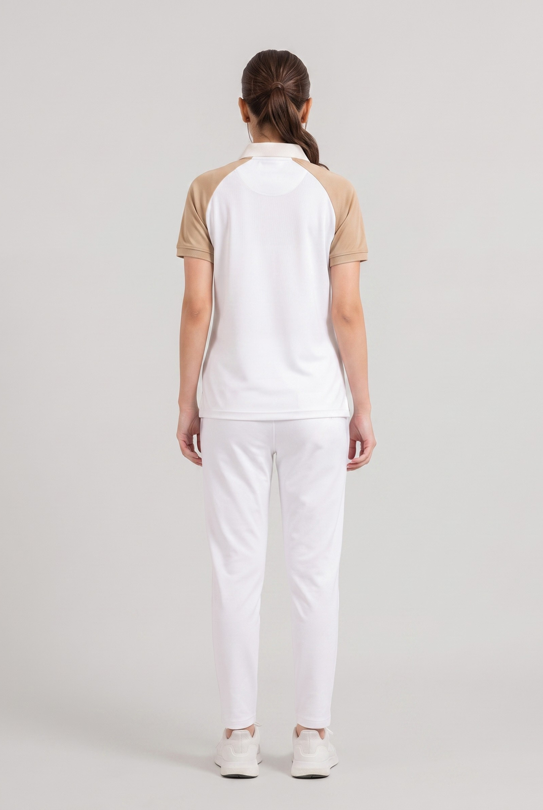 Woman wearing a white polo shirt with beige sleeves and white pants on a light gray background