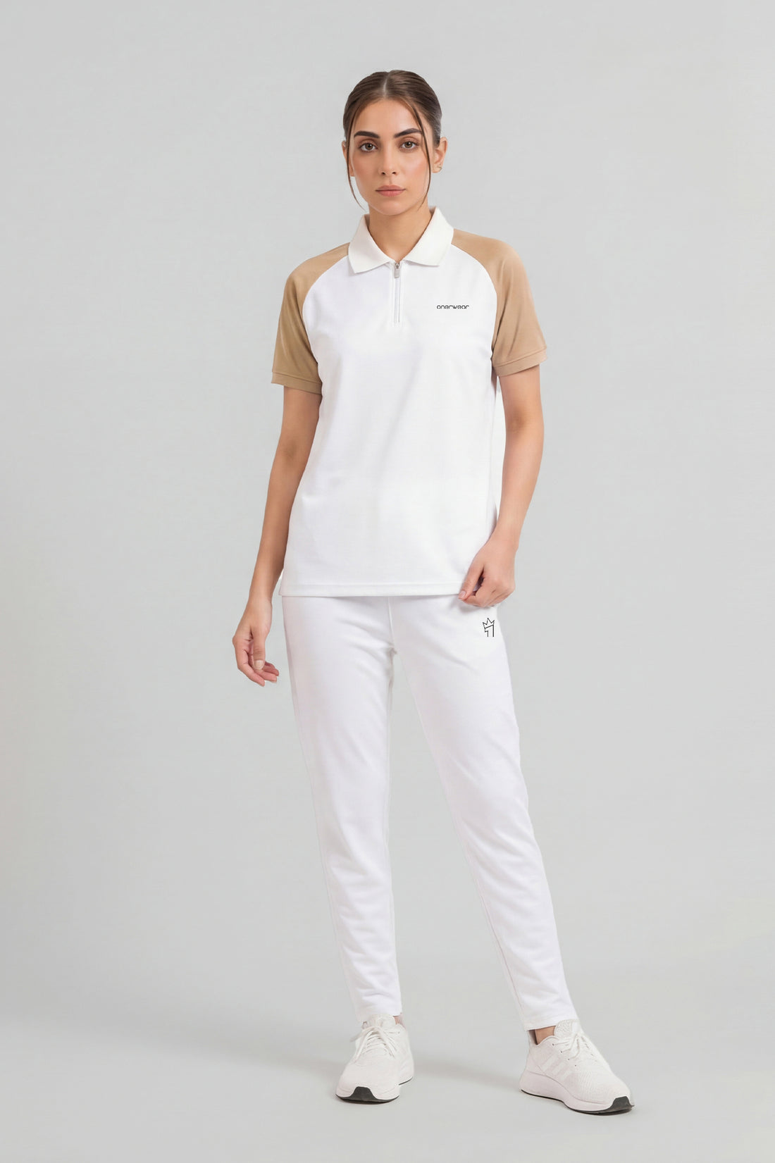 Woman wearing a white polo shirt with beige sleeves and white pants on a light gray background