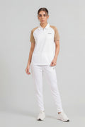 Woman wearing a white polo shirt with beige sleeves and white pants on a light gray background