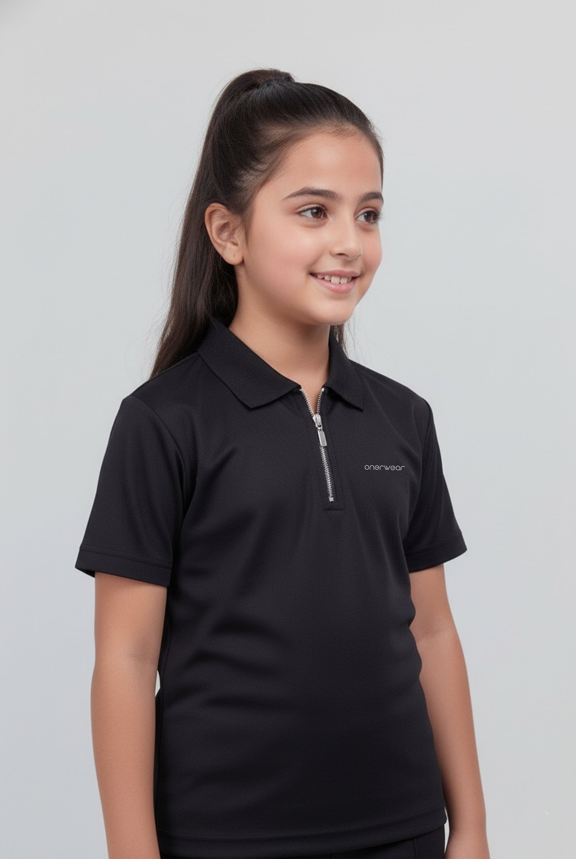 Young girl wearing a black polo shirt with a logo on a light gray background