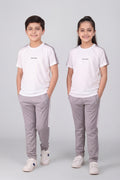 Two children wearing matching white t-shirts and gray pants on a plain background