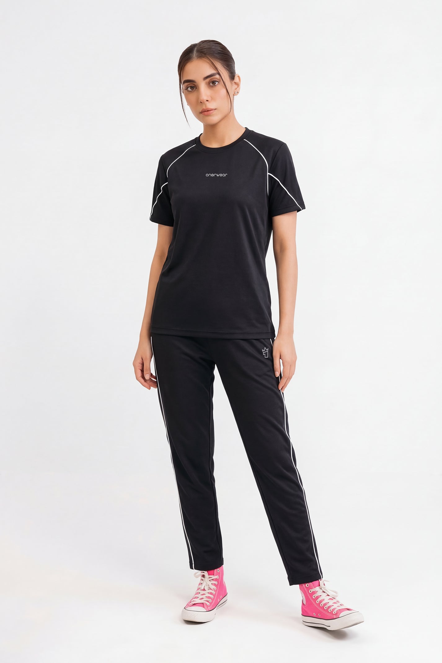 Woman wearing a black athletic outfit with pink shoes on a white background