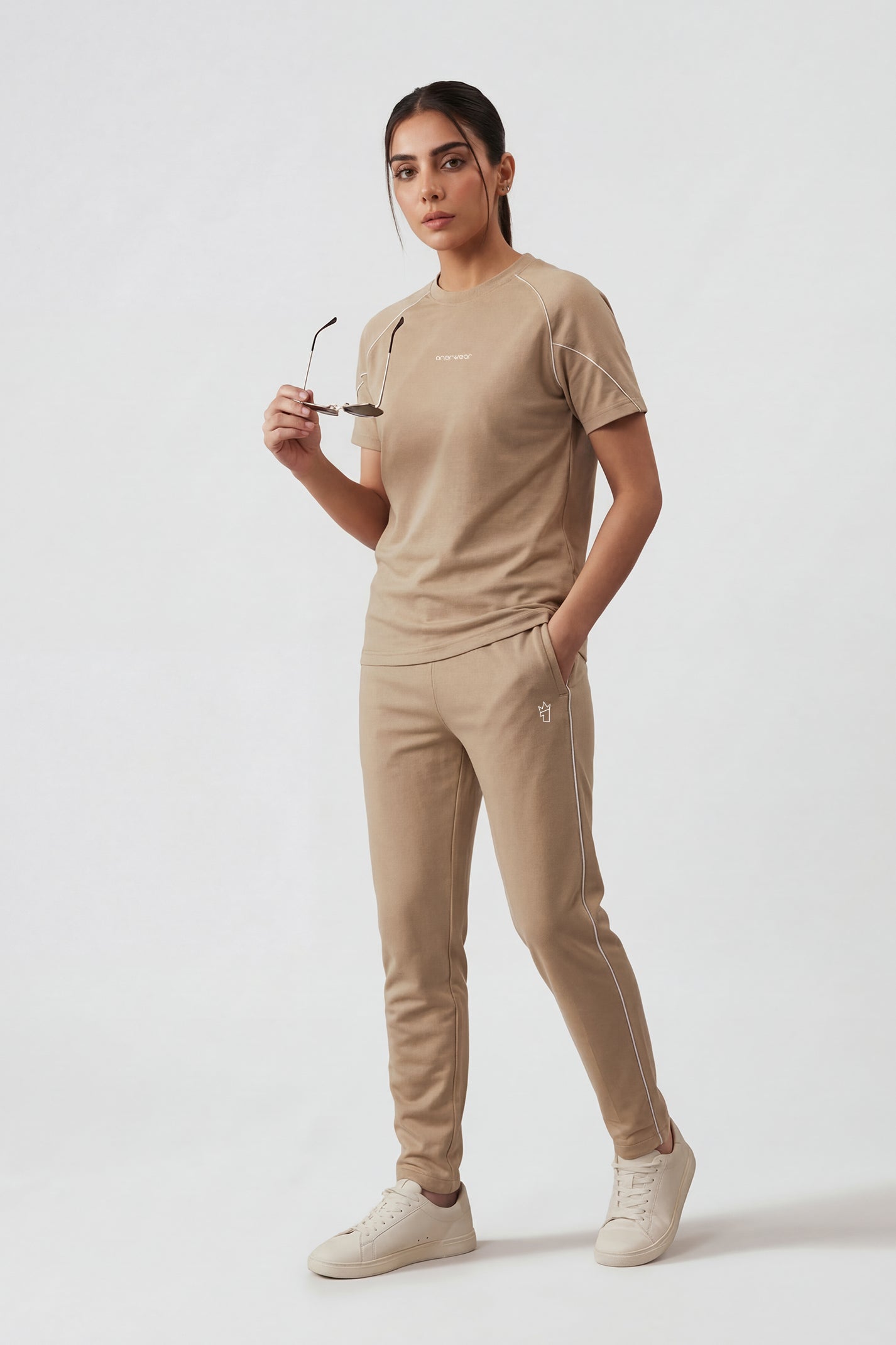 Woman wearing a beige outfit with sunglasses on a white background