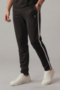 Person wearing black track pants with a white stripe and white sneakers on a gray background