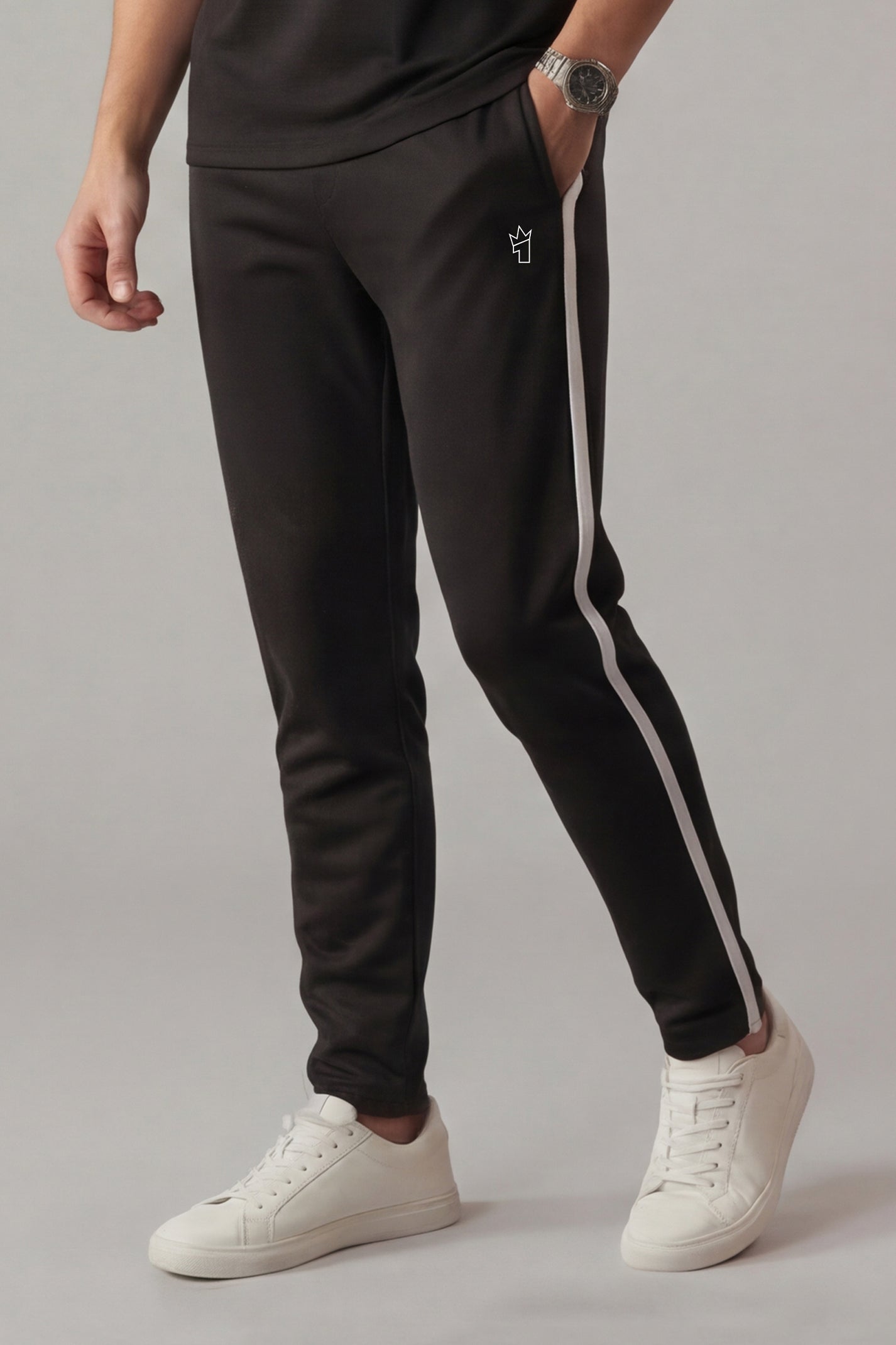 Person wearing black track pants with a white stripe and white sneakers on a gray background