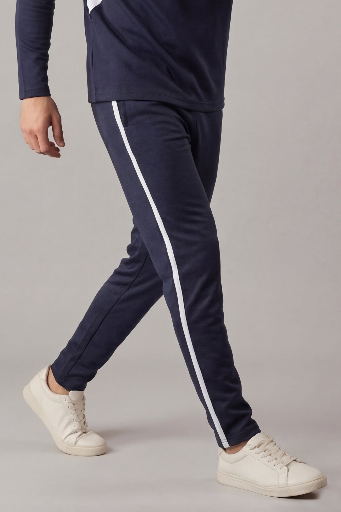 Navy tracksuit with white stripes worn by a person on a gray background