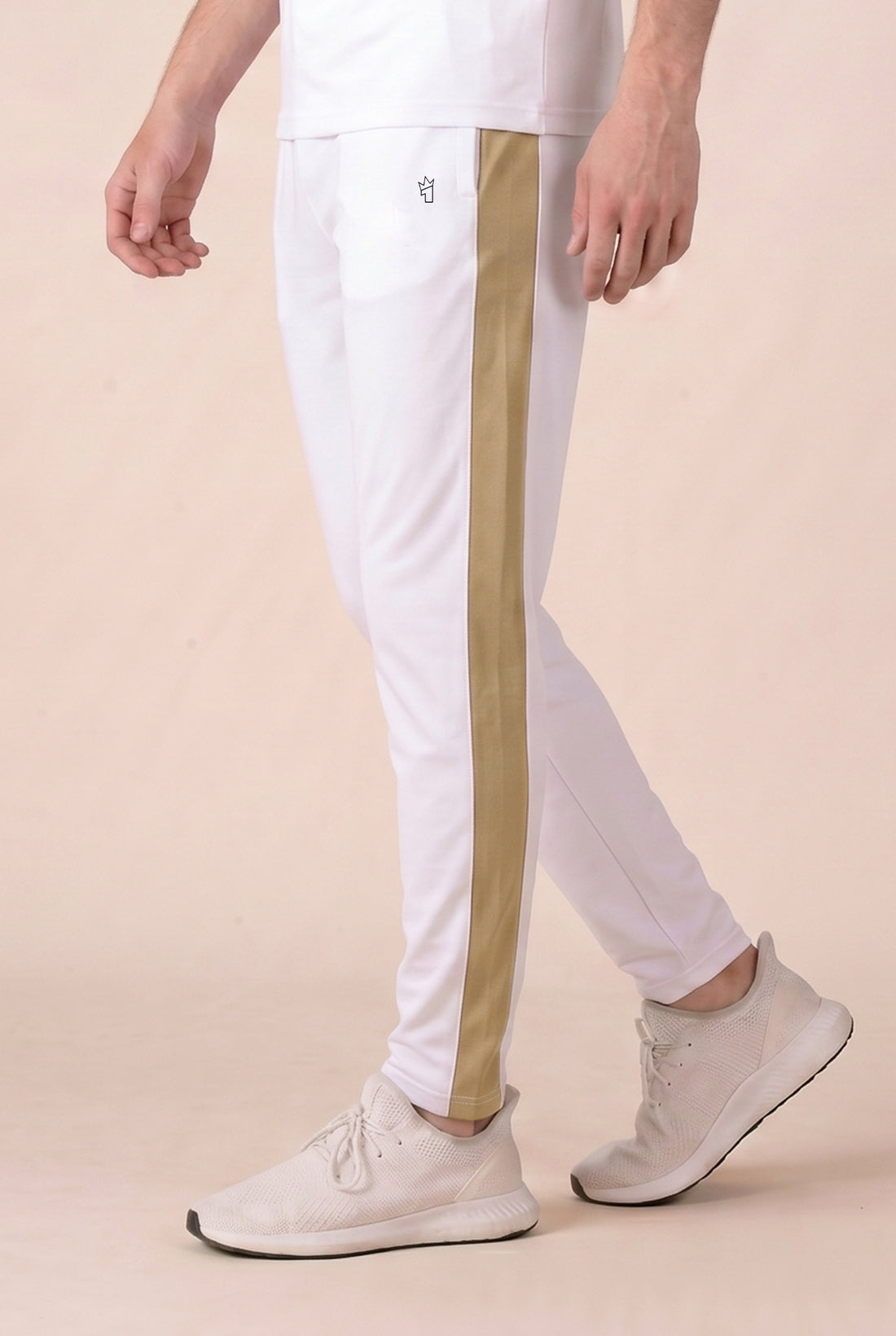 Man wearing a white polo shirt with brown sleeves and white pants on a beige background